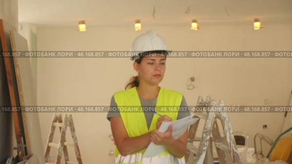Woman foreman in a protective helmet and yellow vest checks the completed construction work on the drawing. Стоковое видео, видеограф Яков Филимонов / Фотобанк Лори