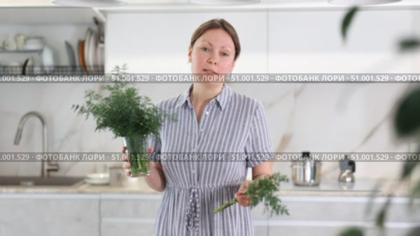 Woman in dress with short sleeves sitting near kitchen table and holding glass with bunch of dill. Стоковое видео, видеограф Яков Филимонов / Фотобанк Лори