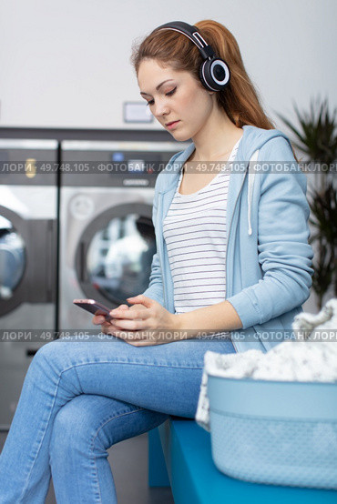 woman in laundromat using smartphone and wearing headphones. Стоковое фото, агентство Ingram Publishing / Фотобанк Лори