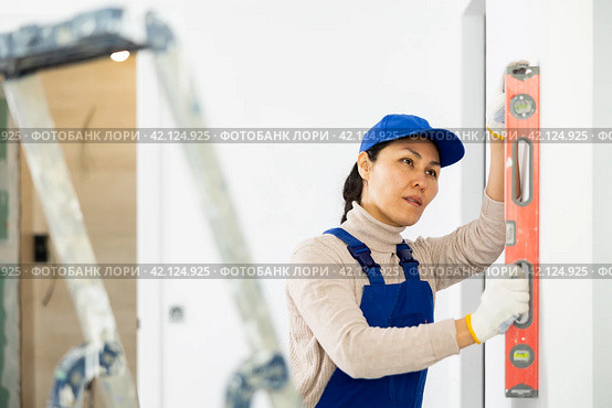 Woman in overalls checks the verticality of walls with a building level. Стоковое фото, фотограф Яков Филимонов / Фотобанк Лори