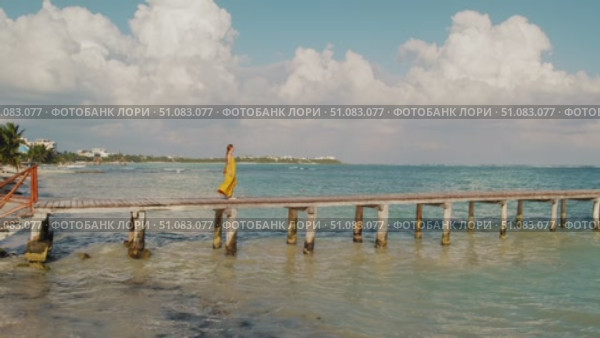 Woman in summer dress walks on wooden pier over turquoise ocean water in Mexico. Стоковое видео, видеограф Ольга Сухарева / Фотобанк Лори