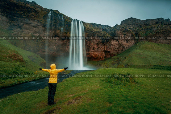 Woman in yellow with arms raised on the Seljalandsfoss waterfall, Iceland. Стоковое фото, агентство Ingram Publishing / Фотобанк Лори