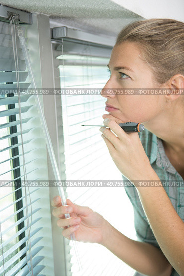 woman installing blinds with screwdriver. Стоковое фото, агентство Ingram Publishing / Фотобанк Лори