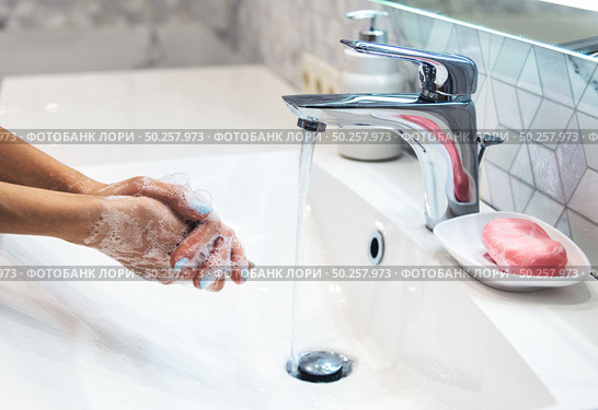 Woman is washing hands with soap and hot water at home bathroom sink. Girl is cleaning hands. Hygiene for coronavirus outbreak prevention. Covid-19 pandemic protection by washing hands frequently. Стоковое фото, агентство Ingram Publishing / Фотобанк Лори