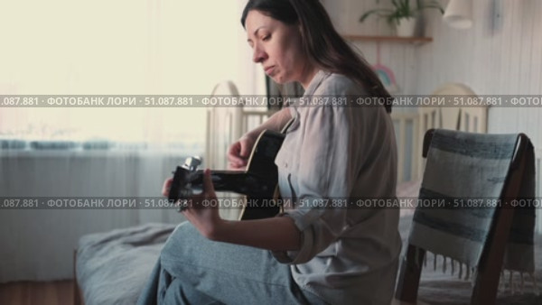 Woman Practicing Guitar in Cozy Room at Home. Strumming black acoustic guitar. Female learning to play music. Person hand on a guitar neck. Guitarist working on melody, performance, practice indoors. Стоковое видео, видеограф Марина Демидюк / Фотобанк Лори