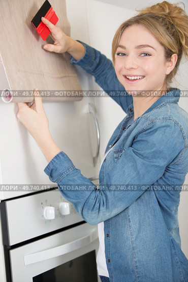 woman refurbishing kitchen cupboard with adhesive material. Стоковое фото, агентство Ingram Publishing / Фотобанк Лори