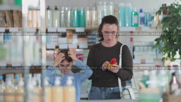 Woman stands in a pharmacy and checks her daughter's hair for lice. Child stands in the pharmacy with mother in search of remedies and shampoos for lice. Стоковое видео, видеограф Яков Филимонов / Фотобанк Лори
