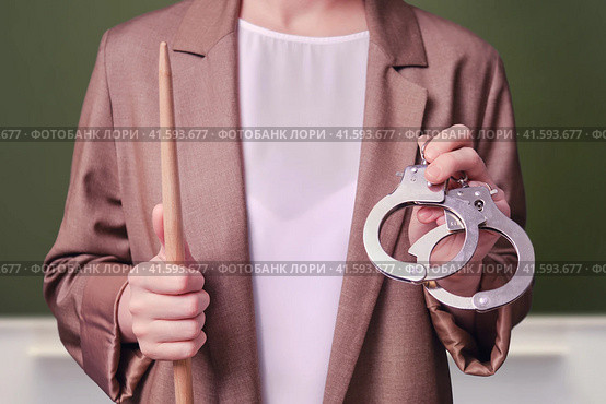 Woman teacher holding handcuffs in her hands on school blackboard in the classroom. Стоковое фото, фотограф Андрей Журавлев / Фотобанк Лори
