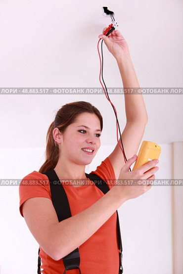 Woman using a voltmeter on ceiling electrics. Стоковое фото, агентство Ingram Publishing / Фотобанк Лори