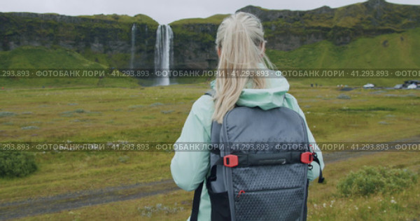 Woman with backpack enjoying impressive Seljalandsfoss waterfall in Iceland. Стоковое видео, видеограф Igor Tichonow / Фотобанк Лори