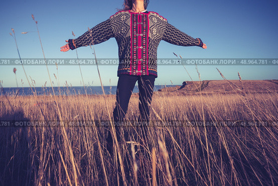 Woman with her arms raised in a field by the sea at sunset. Стоковое фото, агентство Ingram Publishing / Фотобанк Лори