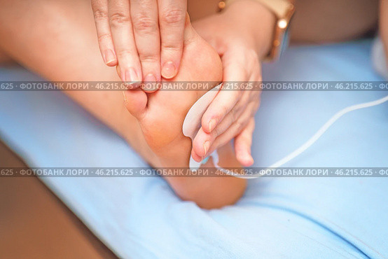 Woman's hands are attaching an electrode from a muscle stimulator to her foot, preparing for a muscle training session. Focus on fitness, wellness, and technology. Стоковое фото, фотограф Татьяна Степанищева / Фотобанк Лори