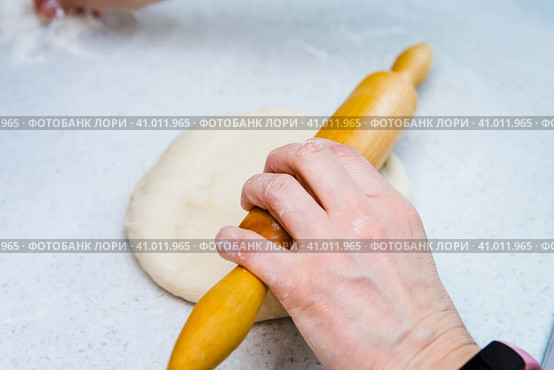 Woman's hands with a dough. A woman rolls out a piece of dough with a wooden rolling pin. She takes a pinch of flour by another hand. Женские руки с тестом. Женщина раскатывает кусок теста деревянной скалкой. Другой рукой она берет щепотку муки. Стоковое фото, фотограф Дмитрий Березнев / Фотобанк Лори