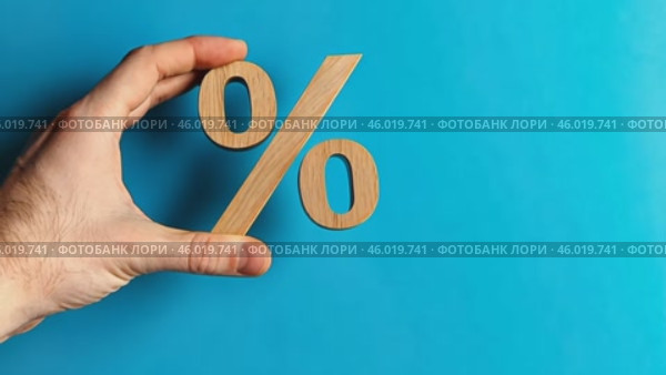 Wood percentage sign in a human hand. Blue studio background, copy space. Symbol percent. Seasonal sale, discount. Rate for finance, return. Investment ROI, credit, mortgage, tax, marketing, promotion. Стоковое AI-видео, аниматор Марина Демидюк / Фотобанк Лори