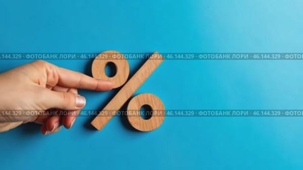Wood percentage sign in a human hand. Blue studio background, copy space. Symbol percent. Seasonal sale, discount. Rate for finance, return. Investment ROI, credit, mortgage, tax, marketing, promotion. Стоковое AI-видео, аниматор Марина Демидюк / Фотобанк Лори