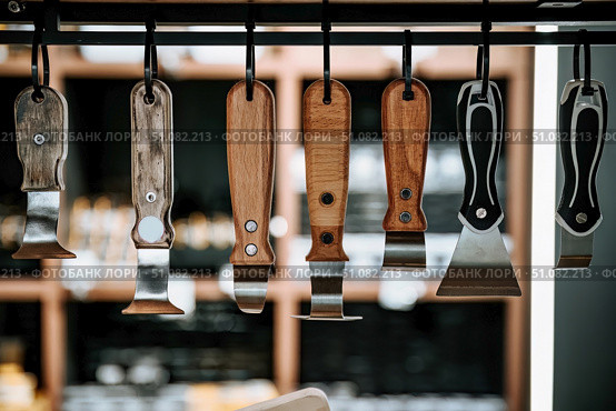Wooden and plastic handled spatula tools hanging on display in a hardware store, used for stretch ceiling installation and PVC film fitting. Стоковое фото, фотограф Татьяна Терехина / Фотобанк Лори