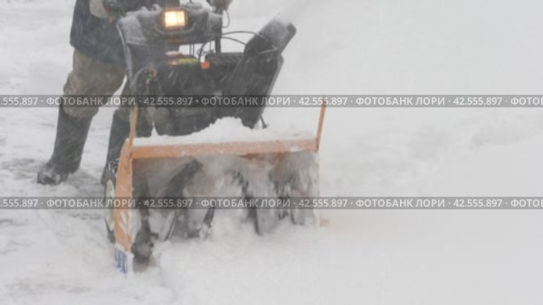 Worker using snow blower to remove snowdrift during winter snowy storm. Mechanized snow removal from road during powerful cyclone (2024 год). Редакционное видео, видеограф А. А. Пирагис / Фотобанк Лори