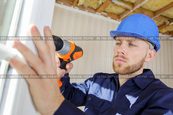 workman using cordless drill while installing pvc windows. Стоковое фото, агентство Ingram Publishing / Фотобанк Лори