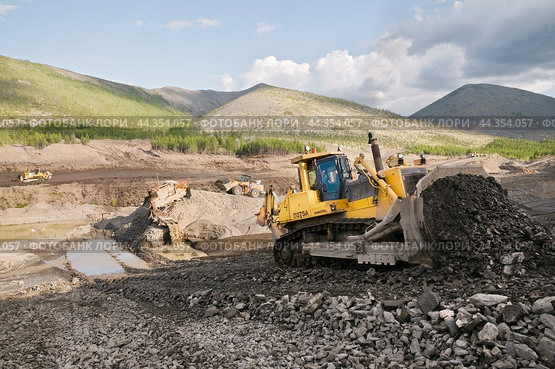 Японский Бульдозер Komatsu D375 в горной местности,сгребает от промывочного устройства отработанный горный грунт, чтобы затем его сгрести ковшом в отвал. На дальнем плане - стационарное промывочное устройство для промывки золота (2009 год). Редакционное фото, фотограф Павел Просянов / Фотобанк Лори