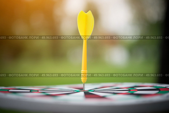 Yellow dart arrow hitting in the center of dartboard. Стоковое фото, агентство Ingram Publishing / Фотобанк Лори