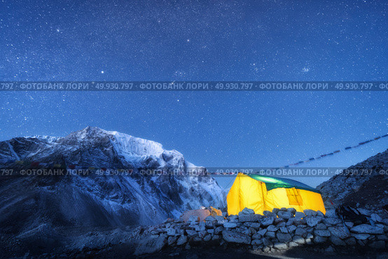 Yellow glowing tent against high rocks with snowy peak and sky with stars at night in Nepal. The Himalayan Mountains. Landscape with mountains, starry sky and bivouac. Trekking in Himalayas. Travel. Стоковое фото, агентство Ingram Publishing / Фотобанк Лори