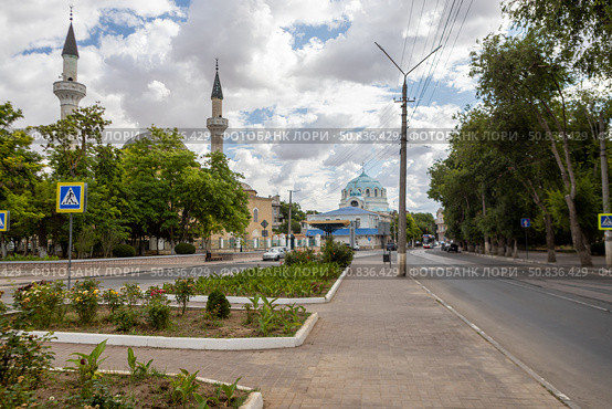 Yevpatoria, Russian Federation - July 05, 2025: Scenic street view featuring lush greenery, traditional architecture, and minarets under a cloudy sky, capturing the essence of urban tranquility. Редакционное фото, фотограф Ирина Ручушкина / Фотобанк Лори