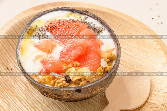 Yogurt with grapefruit, granola, chia and honey served in half a coconut shell on a rose marble kitchen countertop. Стоковое фото, агентство Ingram Publishing / Фотобанк Лори