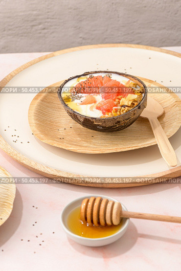 Yogurt with grapefruit, granola, chia and honey served in half a coconut shell on a rose marble kitchen countertop. Стоковое фото, агентство Ingram Publishing / Фотобанк Лори