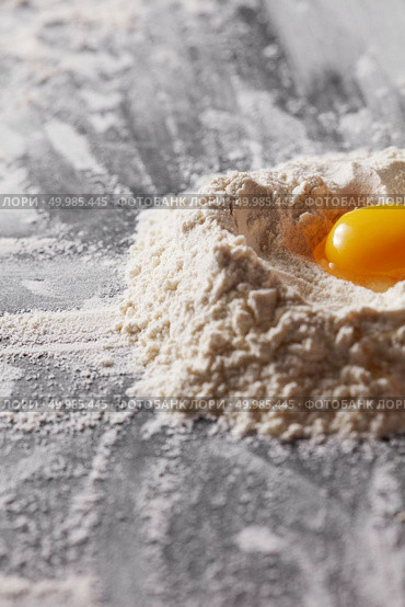 Yolk in organic flour on the kitchen table. Ingredients for home baking. Fresh egg and flour on the kitchen table. Preparation for kneading the dough. Стоковое фото, агентство Ingram Publishing / Фотобанк Лори