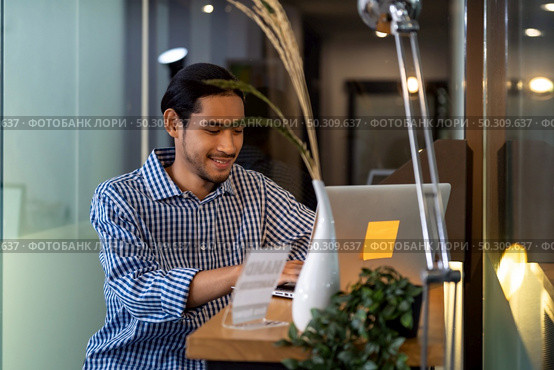 Young adult Asian businessman sitting at coffee bar in office with laptop. Smart office work everywhere concept. Стоковое фото, агентство Ingram Publishing / Фотобанк Лори