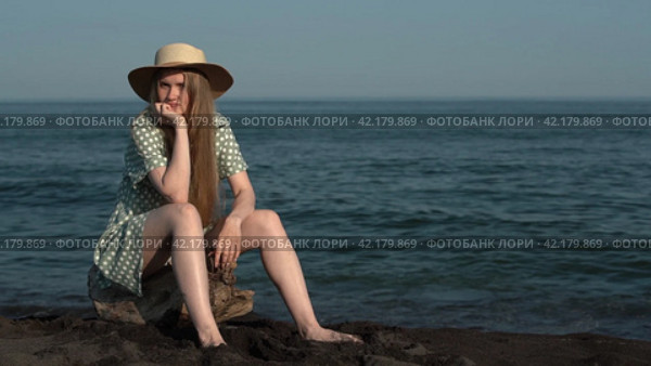Young adult blonde sitting on log on beach on background of ocean waves. Cinematic shot. Стоковое видео, видеограф А. А. Пирагис / Фотобанк Лори