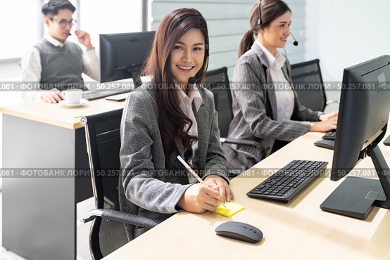 Young adult friendly and confidence operator woman agent smiling with headsets working in call centre with her colleague team working. Стоковое фото, агентство Ingram Publishing / Фотобанк Лори