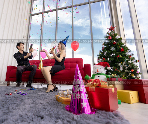 Young asian adult couple celebrating New year and Christmas holiday together with Firecrackers and confetti in living room of big apratment with christmas tree decoration. Стоковое фото, агентство Ingram Publishing / Фотобанк Лори