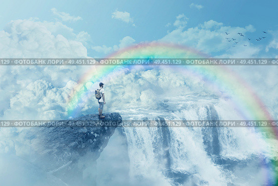 Young boy on a cliff looking at the horizon with a waterfall above clouds. Life journey below a rainbow in paradise. Inspirational imaginary view. . Стоковое фото, агентство Ingram Publishing / Фотобанк Лори