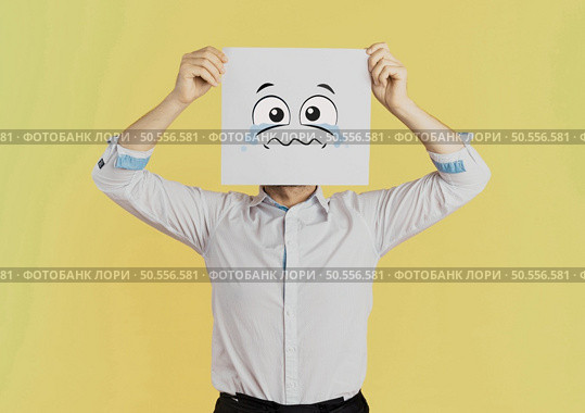 Young businessman holding white card with a sad face on it isolated on Yellow background. Стоковое фото, агентство Ingram Publishing / Фотобанк Лори