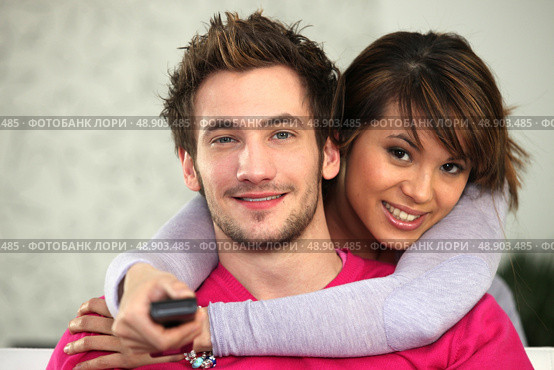Young couple watching TV with a remote control. Стоковое фото, агентство Ingram Publishing / Фотобанк Лори