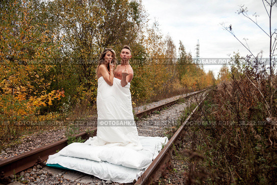 Young cute couple on their honeymoon woman and man embrace in their bed on railway tracks. Concept of romantic travel ban and inability to move. Stay at home. Copying space for a site. Стоковое фото, фотограф Aleksandr Golubev / Фотобанк Лори