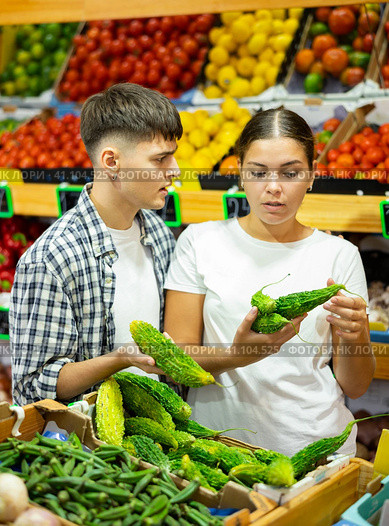 Young family couple chooses fresh bitter melon (Momordica charantia) in grocery supermarket. Стоковое фото, фотограф Яков Филимонов / Фотобанк Лори