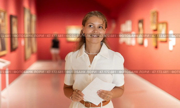 Young girl holding an information booklet looks at paintings in an art exhibition in museum. Стоковое фото, фотограф Яков Филимонов / Фотобанк Лори