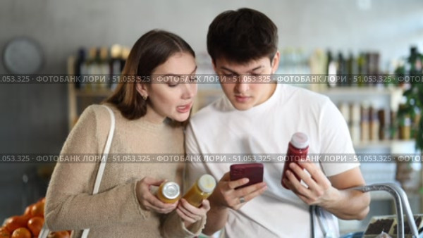 Young girl with husband in big supermarket scan QR code bottle of smoothie. Couple of buyers friends take photo information on packaging of bio product. Стоковое видео, видеограф Яков Филимонов / Фотобанк Лори