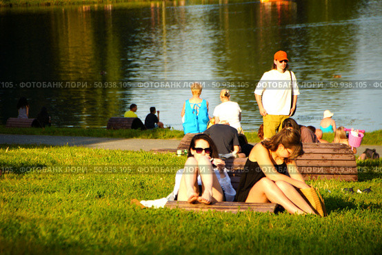 Young girls sunbathing on a green lawn on the shore of a pond in Kuzminki Park. Russia. Moscow. 25.07.25. Редакционное фото, фотограф Ярославский Максим / Фотобанк Лори