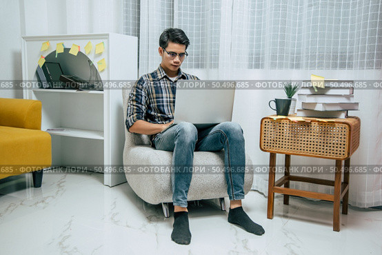 Young handsome man wearing eyeglasses with new normal, Stay at home and works from home on laptop computer while self-isolation and quarantine covid-19 coronavirus outbreak. Стоковое фото, агентство Ingram Publishing / Фотобанк Лори