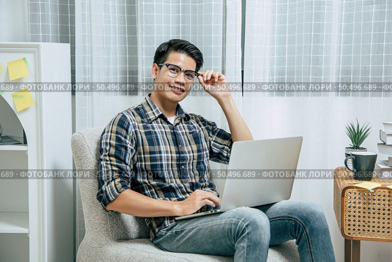 Young handsome man wearing eyeglasses with new normal, Stay at home and works from home on laptop computer while self-isolation and quarantine covid-19 coronavirus outbreak. Стоковое фото, агентство Ingram Publishing / Фотобанк Лори