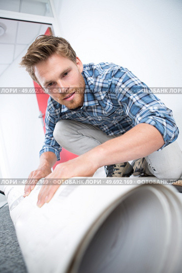 young male worker unrolling carpet on floor at home. Стоковое фото, агентство Ingram Publishing / Фотобанк Лори