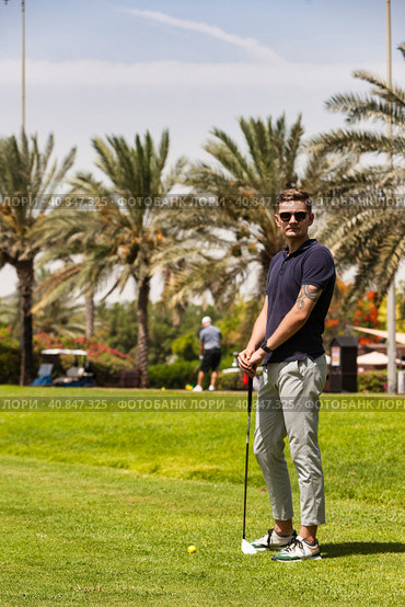 Young man golfer standing on golf course in sportswear and sunglasses, teeing golf club training at palm trees background. Healthy sports lifestyle and leisure activity concept. Copy ad text space. Стоковое фото, фотограф Aleksandr Golubev / Фотобанк Лори