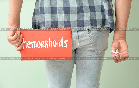 Young man holding paper with text HEMORRHOIDS and suppository on color background. Стоковое фото, фотограф Pixel_shot / Фотобанк Лори