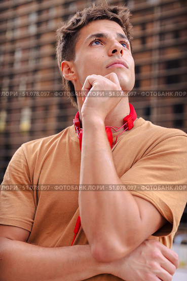 Young man in brown t-shirt with red headphones thinking outdoors in the city. Стоковое фото, фотограф Raquel Corcoles Mendez / Фотобанк Лори