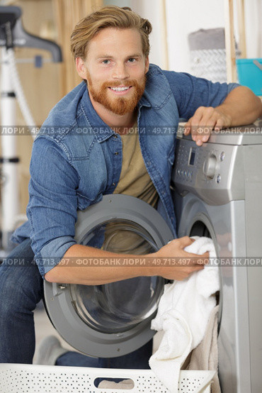young man loading the laundry into the washing machine. Стоковое фото, агентство Ingram Publishing / Фотобанк Лори