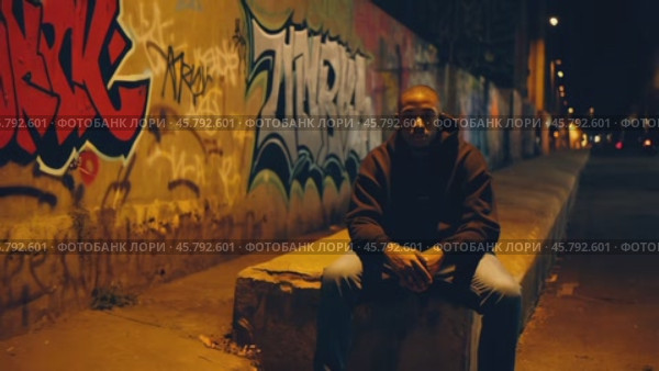 Young man sitting at night in urban street art scenery. Стоковое видео, видеограф Данил Руденко / Фотобанк Лори