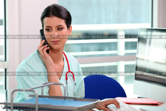 young nurse at phone behind her computer. Стоковое фото, агентство Ingram Publishing / Фотобанк Лори